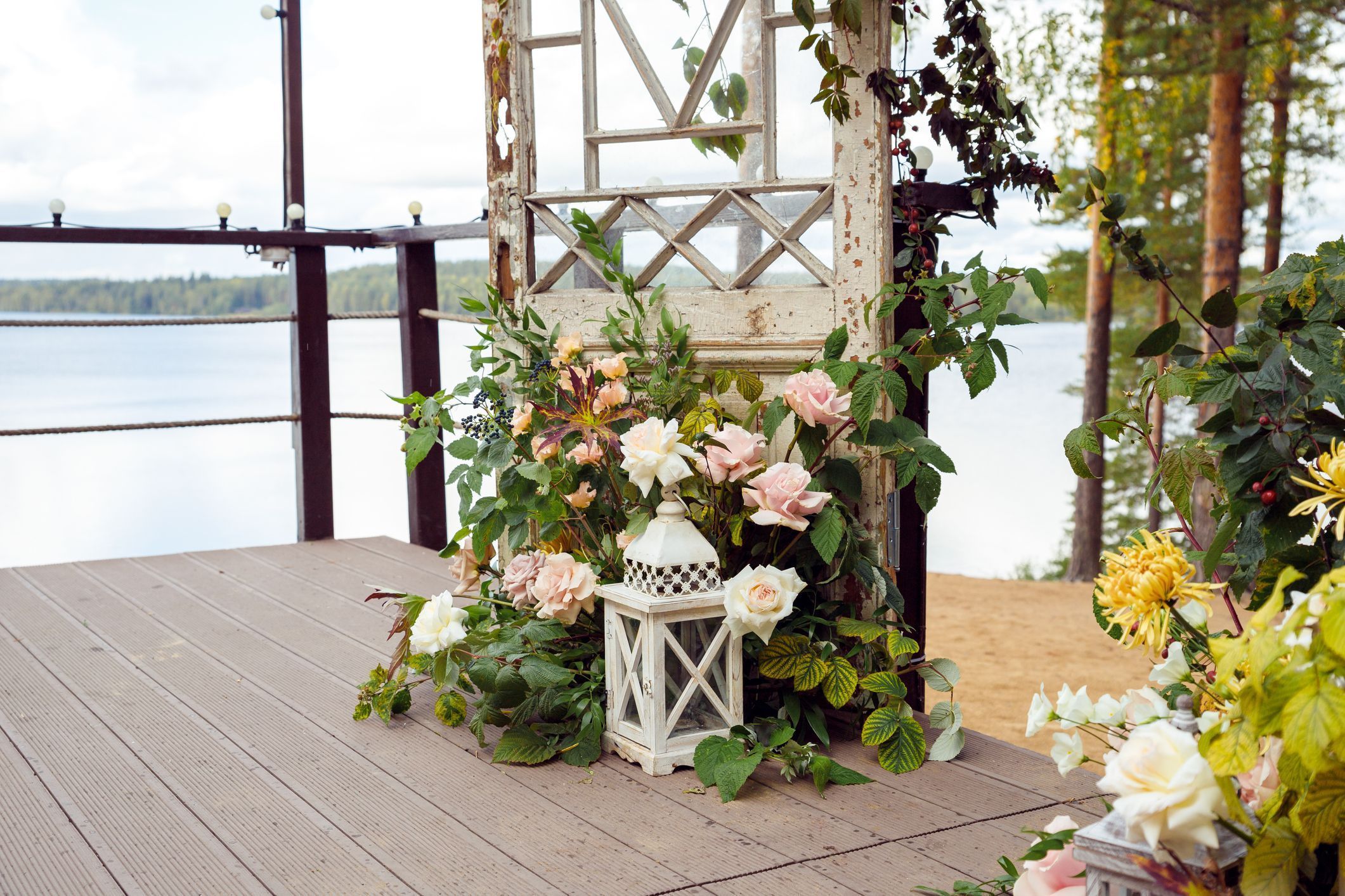 Large white decorative candle lantern, flowers, autumn leaves and old vintage doors on outdoor terrace. Wedding decor, event design. Large white decorative candle lantern, flowers, autumn leaves and old vintage doors on outdoor terrace. Wedding decor, event design.